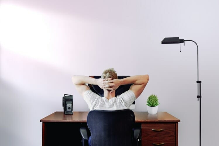 Man sitting in front of a computed with his hands crossed behing his neck